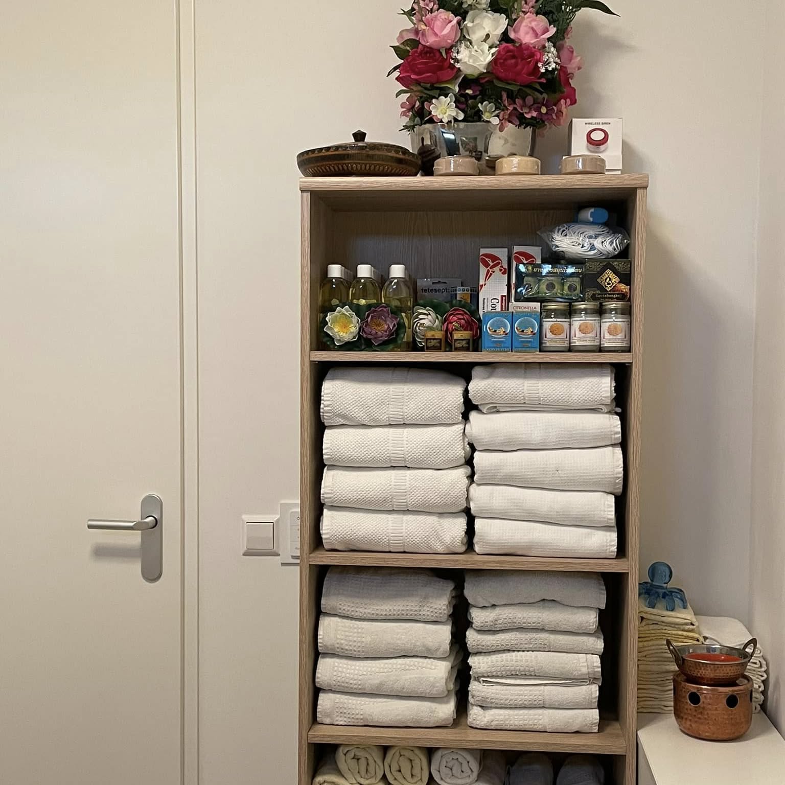 Kast met stapels witte handdoeken, flesjes en bloemen bovenop