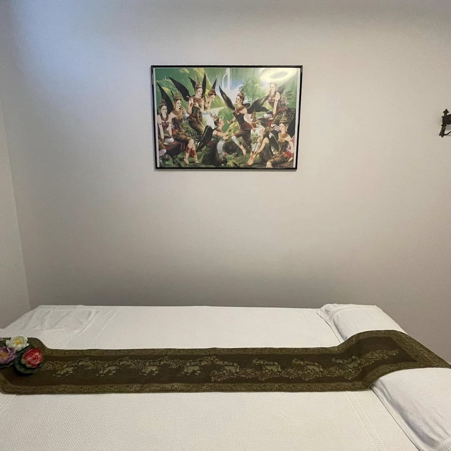 Massagetafel met witte lakens en een gouden tafelloper onder een Thais schilderij