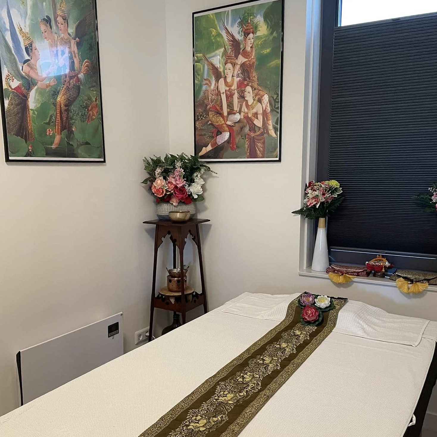 De massagetafel met de gouden tafelloper, Thaise schilderijen en bloemen bij het raam