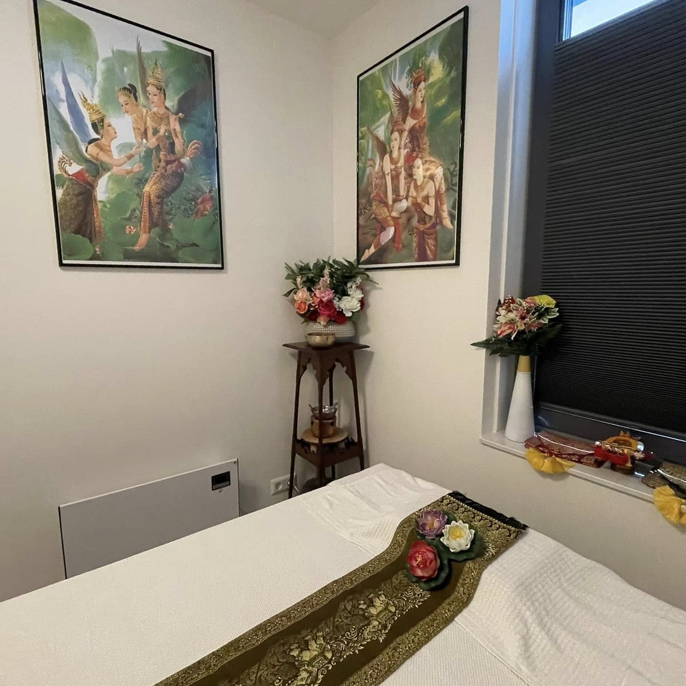 Massagetafel met tafelloper bij het raam, met bloemen in de hoek