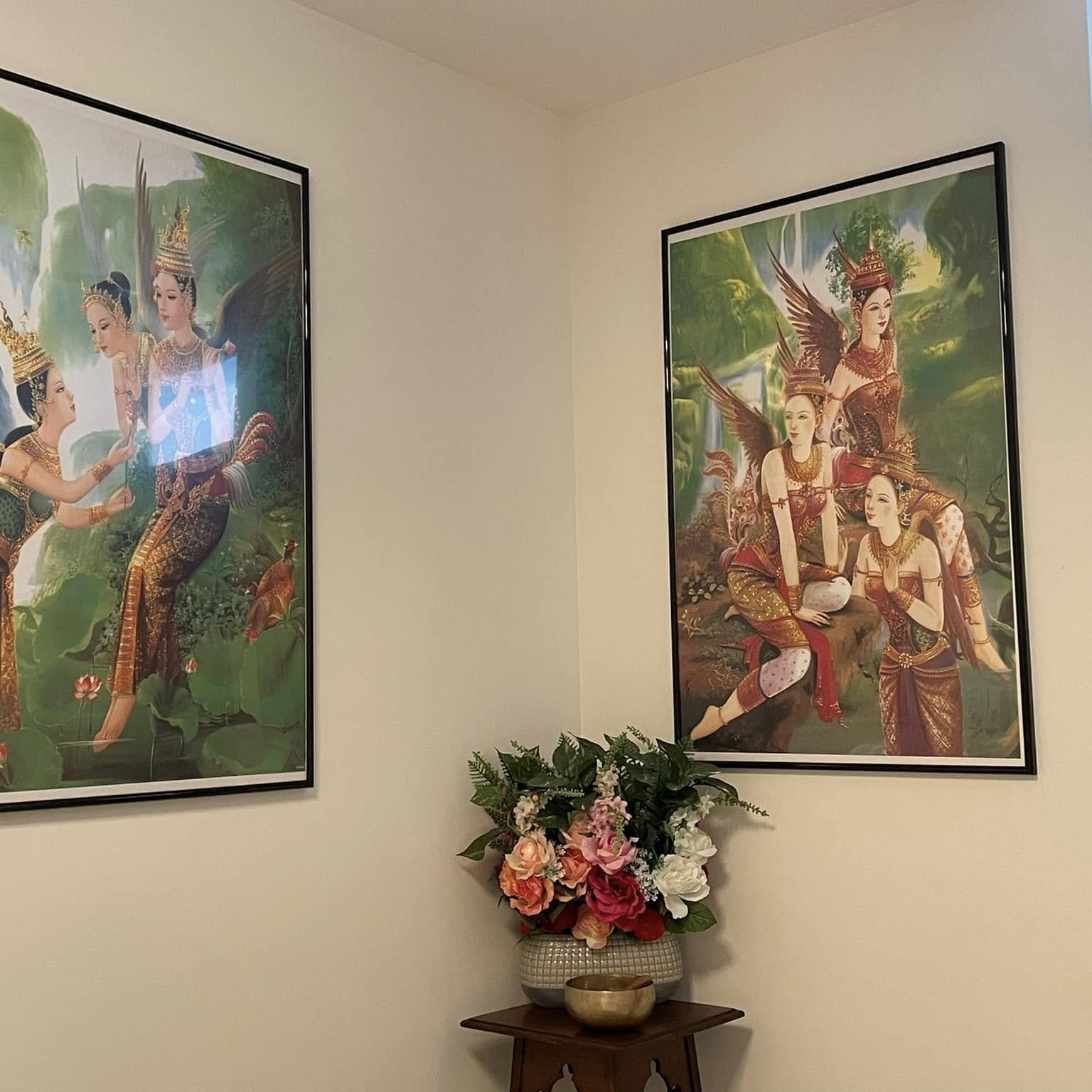 Hoek van de behandelkamer met twee Thaise schilderijen en een bloemstuk op een houten tafeltje